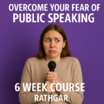 A nervous woman stands in front of a microphone, looking anxious and overwhelmed, with blurred figures of an audience in the background.