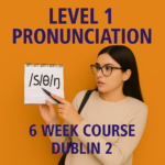 A young woman in glasses points to a notepad showing phonetic symbols /ʃ/, /θ/, /ŋ/. She stands against a bright orange background with the text "Level 1 Pronunciation – 6 Week Course Dublin 2" in bold purple lettering.
